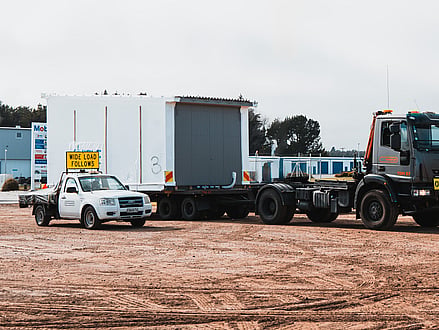 Wide load piloting vehicle with TDM Transport truck moving modular building in Hamilton New Zealand
