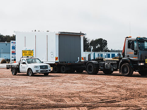 Wide load piloting vehicle with TDM Transport truck moving modular building in Hamilton New Zealand
