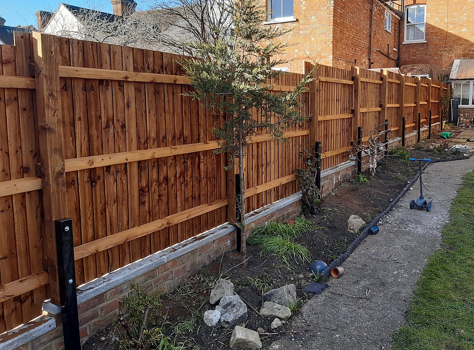 Image shows a timber closeboard fence mounted onto steel spur posts. This enables the fence to project out over the top of a low wall and means the fence follows the boundary. 