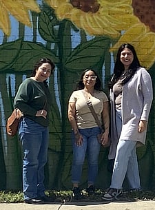 Nancy, Alin, and Zorahila pose in front of sunflower mural