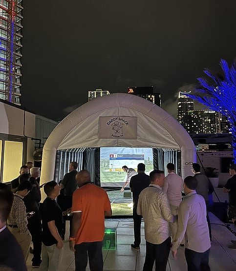 People watching and socializing as man uses mobile golf simulator