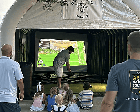 Man showing crowd of children how to use golf simulator and swing golf club
