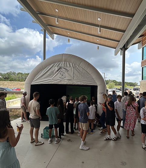 People socializing while watching man use mobile golf simulaotr