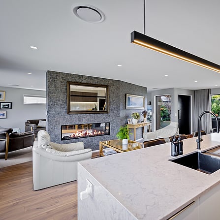 Looking over the stone bench top into the lounge area with timber floors and a gas fireplace.