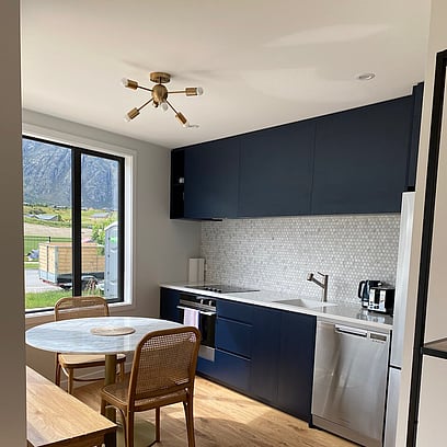 The unit's kitchen with dark navy cabinetry, feature light, tiled splash back, and circle table.