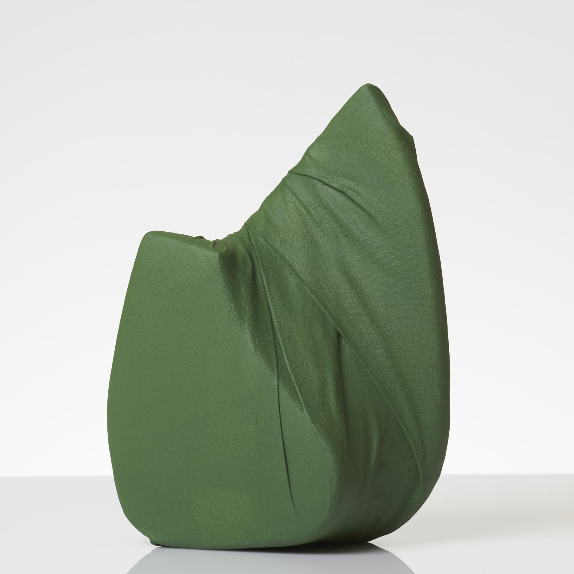 Green small sculpture covered in canvas and painted, there is gentle fold and is shaped with two apex top points. the photo is well lit with the sculpture reflected in the forward shadow in the surface that its is sitting on. 