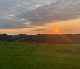 Image of a view from Redwoods Farm across the field with the sun setting over the hill in the distance