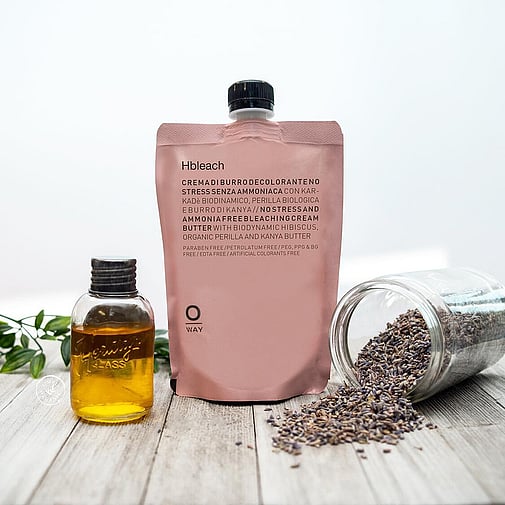 HBleach cream on wooden floor with greenery, apothecary style oil bottle and seeds spilling out of glass jar.