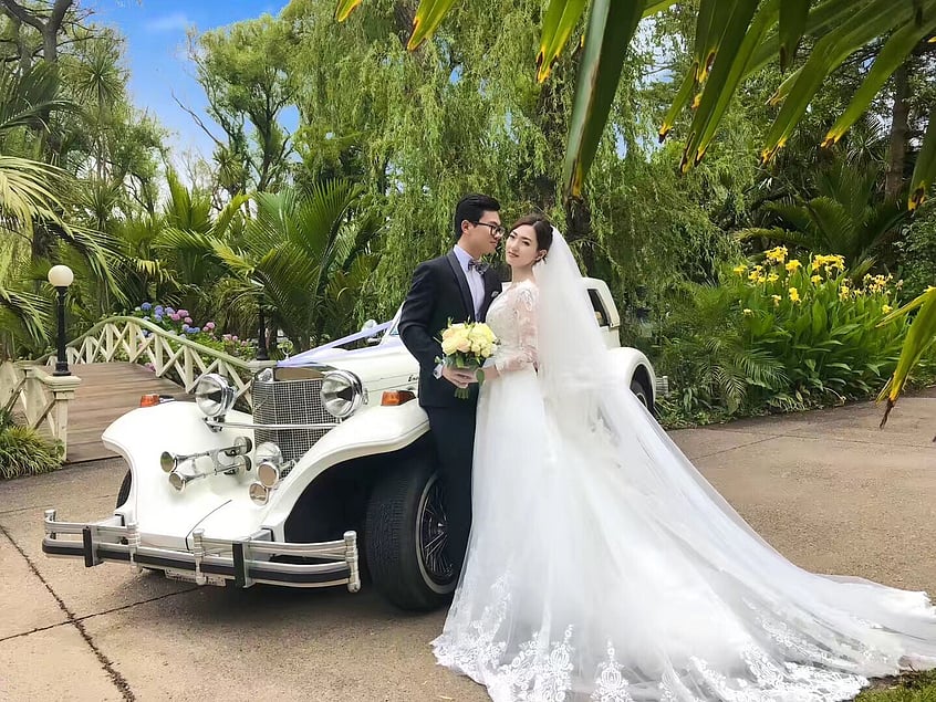 Newlyweds posing beside a vintage wedding car in the gardens at Settlers Country Manor