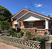 Photo shows the previous 1925 bungalow condition, including non-original white paint and screen block wall