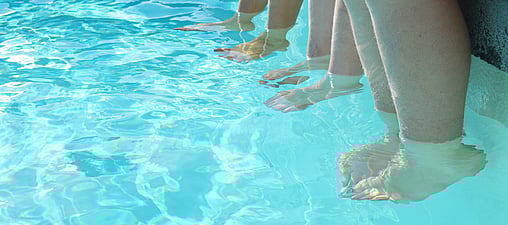 Swimming pool with legs handing over the edge of the pool with feet in the water
