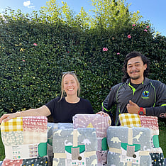 two people smiling for camera standing behind a pile of blankets