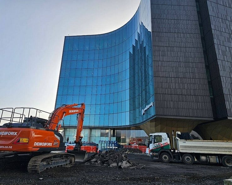 Demoworx excavator working beside a curved glass office building