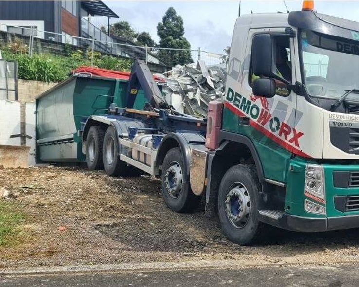 Demoworx hook-lift truck loading a bin of demolition waste