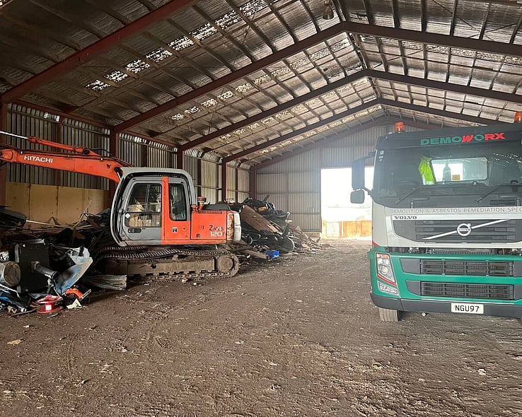Excavator and truck inside a large shed during a commercial demolition