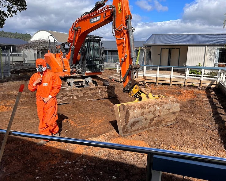 Worker in protective coveralls guiding an excavator on site