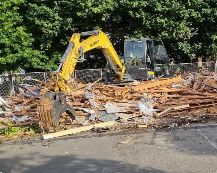 Small excavator sorting timber from a demolished building