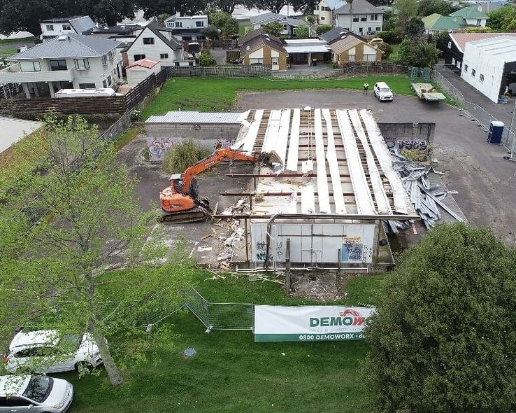 Aerial view of a building being demolished, with a Demoworx sign on the fence