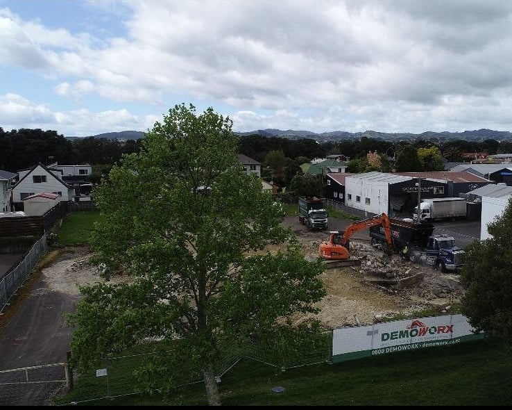 Aerial view of an excavator working beside a large tree on a cleared site