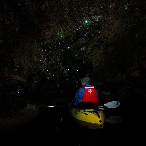 Kayaker paddling through glow worm cave in Rotorua with bioluminescent glow worms lighting up around them