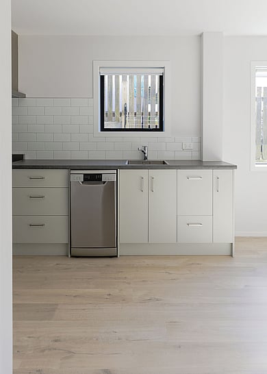 A dark grey kitchen with green tiles and a heavily textured wood look laminate floor. 