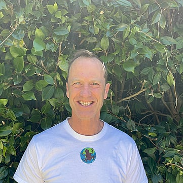 Nik smiling at camera, greenery behind him