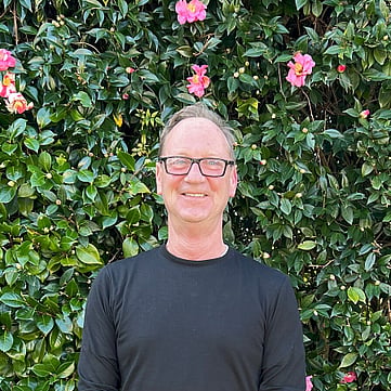 Phil smiling at camera, greenery behind him
