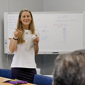 Woman smiling while presenting with a whiteboard behind her