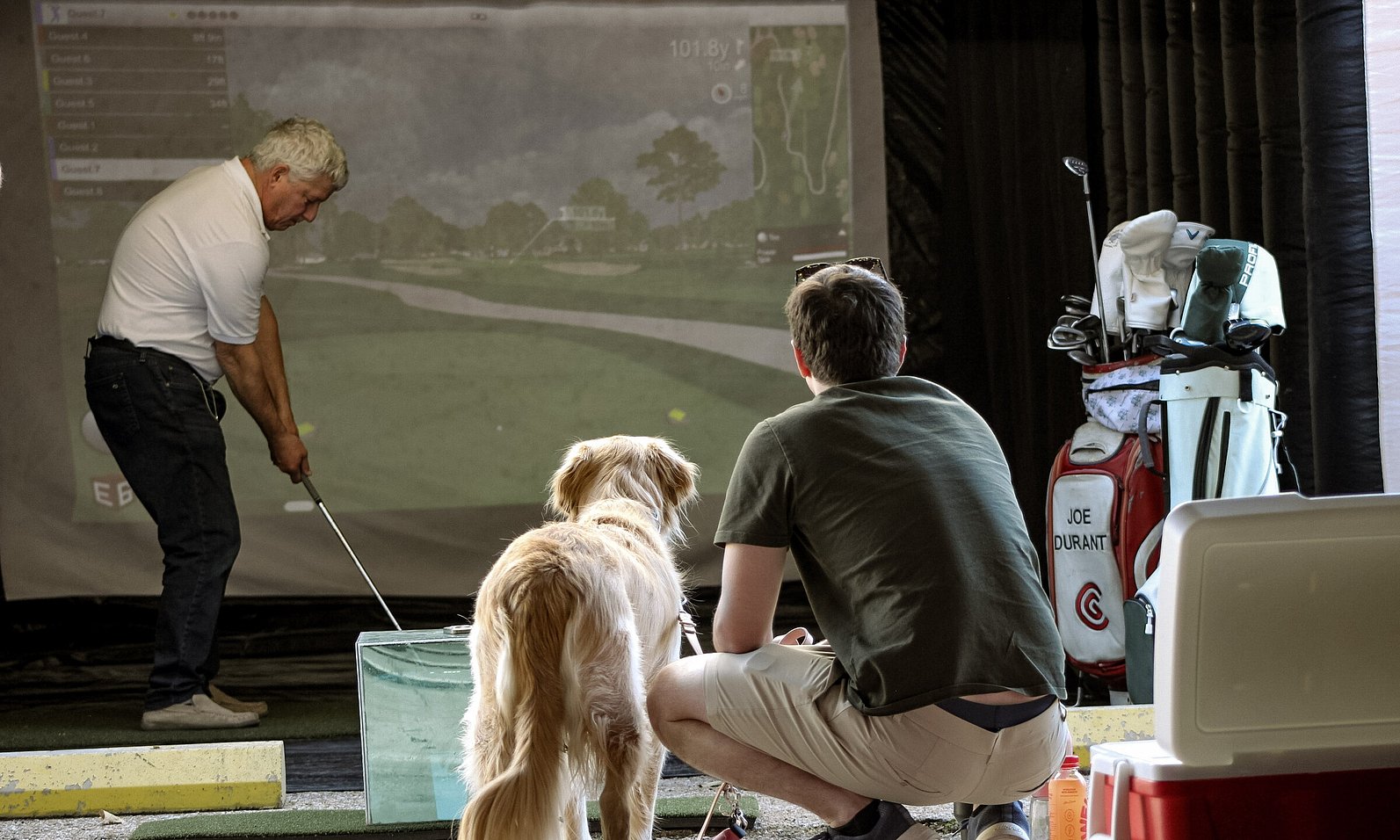 Man and his dog watching someone use the mobile golf simulator