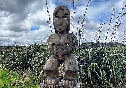 Maori Pou carving in front of flax bushes