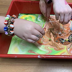 Photo of childs hands swirling paint around in a tray with toothpicks