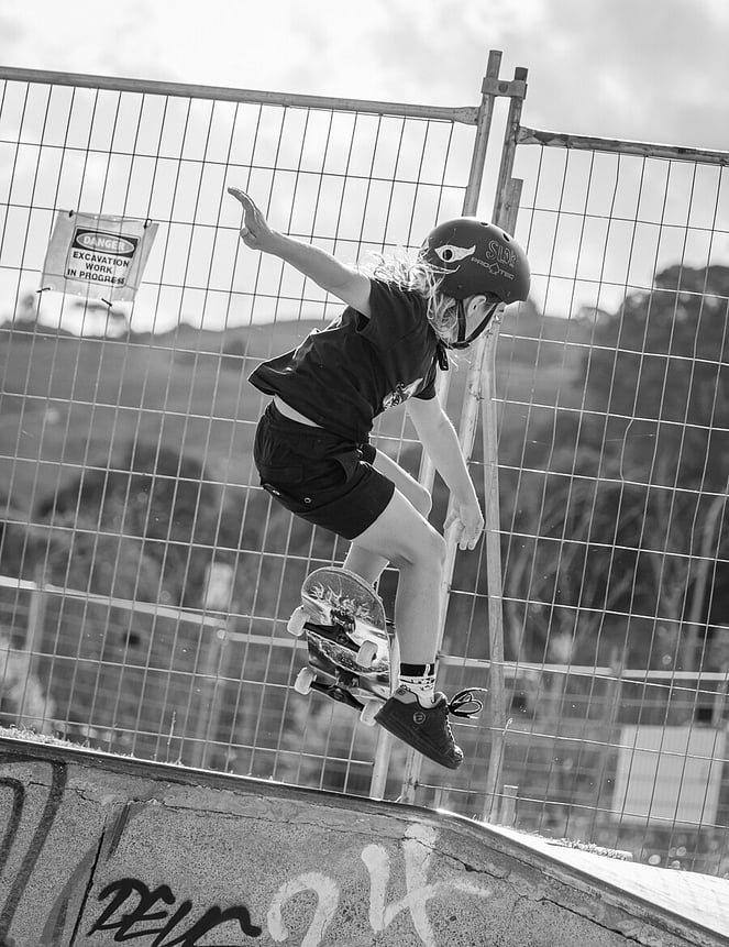 Black and white portrait of a young skateboarder mid-jump with construction in background. 