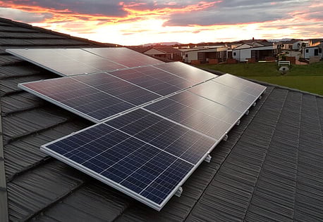 Solar panels on roof in residential area, sunset in background