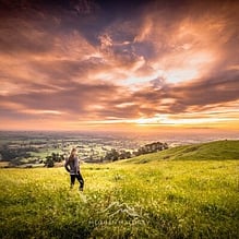 Person standing in a green field under a dramatic sunset sky near Cambridge, Waikato