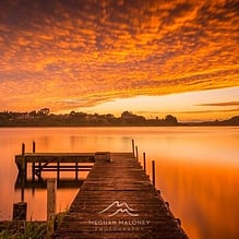 Wooden jetty on a lake under a fiery orange sunset near Cambridge, New Zealand
