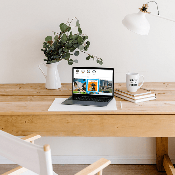 Laptop on a desk with social media marketing open. Plant in vase in the background. Note books with up next to the laptop.