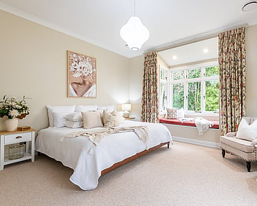 Image of newly renovated master bedroom in sand with floral print curtains and window seat. Renovated by local Te Awamutu residential builders, Whitechurch Construction.