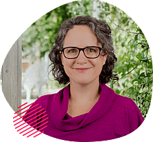 Smiling woman with short curly hair and glasses, wearing a magenta top, framed by a rounded shape with pink accents, standing outdoors