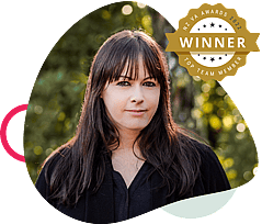 Woman with long dark hair in a black top, framed by a rounded shape with pink and beige accents and a gold Top Team Member badge