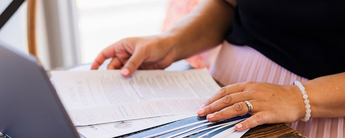 Close-up of Sarah reviewing a stack of printed CVs at a wooden desk with a laptop and smartphone, representing CV writing services by CVs by Sarah.