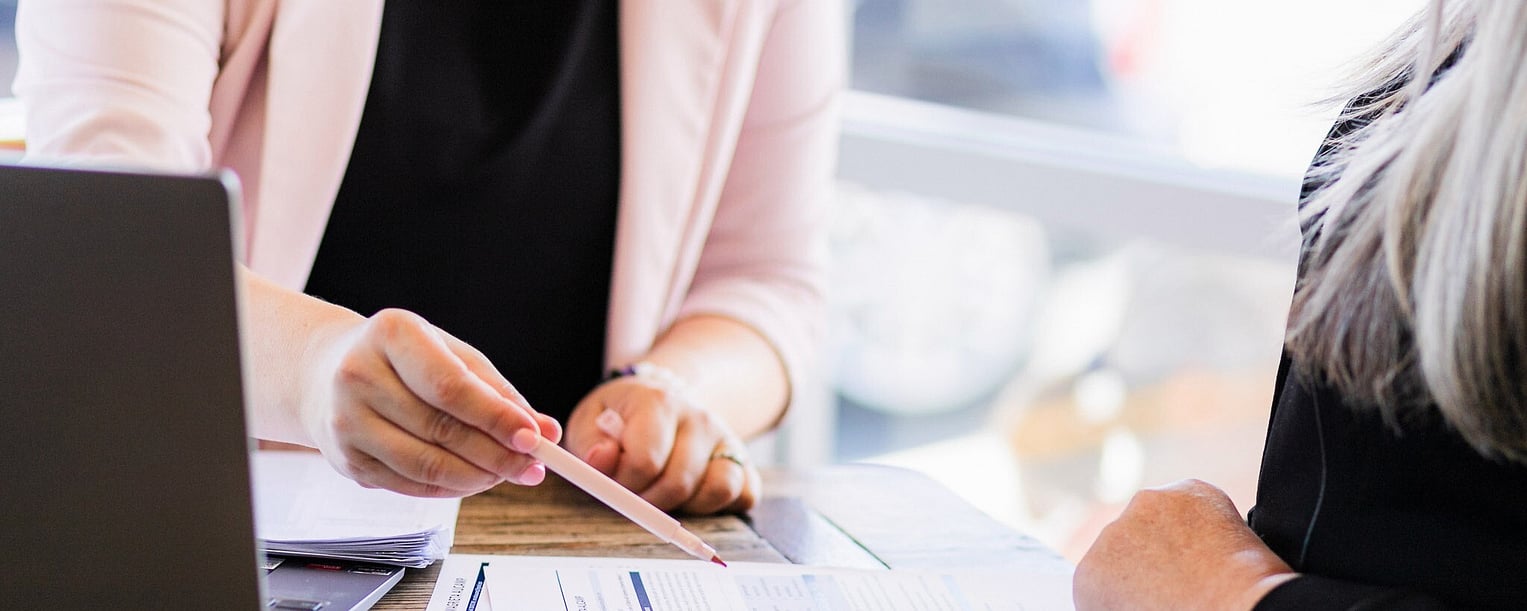 A CV writing consultant reviews a client&rsquo;s resume at a wooden table, highlighting key points with a pen during a one-on-one career consultation.