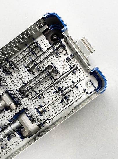 A top view of a surgical instrument tray containing various tools used for robotic-assisted joint replacement surgery, neatly arranged in a sterilised container with blue and metal accents.