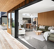 Coastal‑style living room with timber accents and polished concrete floor — Kōtare Grove