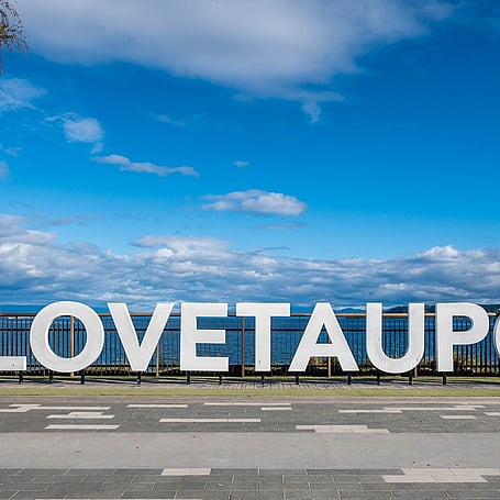 #LOVETAUPO" sign on the lakefront promenade with blue sky and lake views