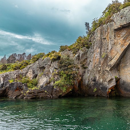 Rocky cliff face and native bush meeting the turquoise waters of Lake Taupo