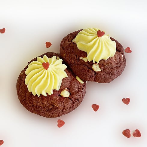 Delicious looking red velvet white chocolate chip cookies filled with cream cheese icing with edible small red heart decorations