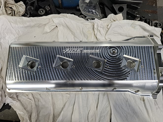 Machined aluminium part with concentric toolpath patterns and two rectangular openings, engraved with &ldquo;RUSE&rdquo; logo.
