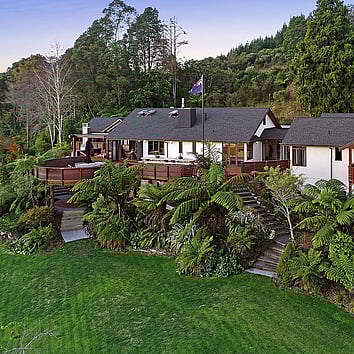 large home surrounded by new zealand native trees. A flag pole and new zealand flag is on the deck. 