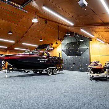 Modern fishing boat on a trailer in a large timber garage. Black climbing wall on the far side.