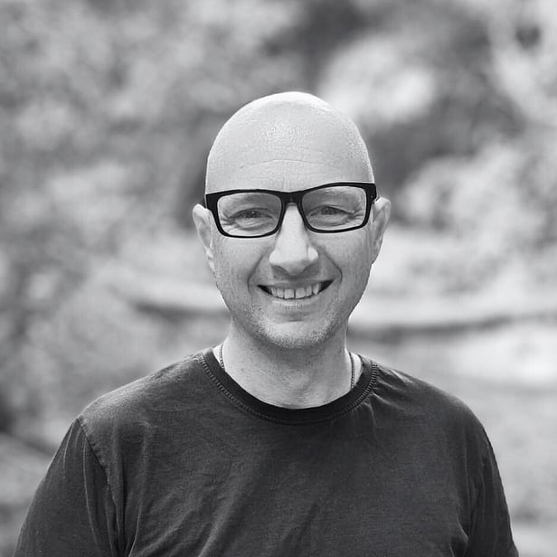 Man with bald head, glasses and a dark t-shirt stood in nature. Black and white photo. 
